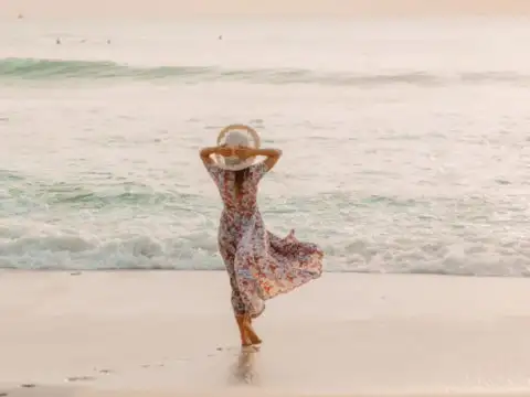 Woman standing by ocean in a dress and sunhat