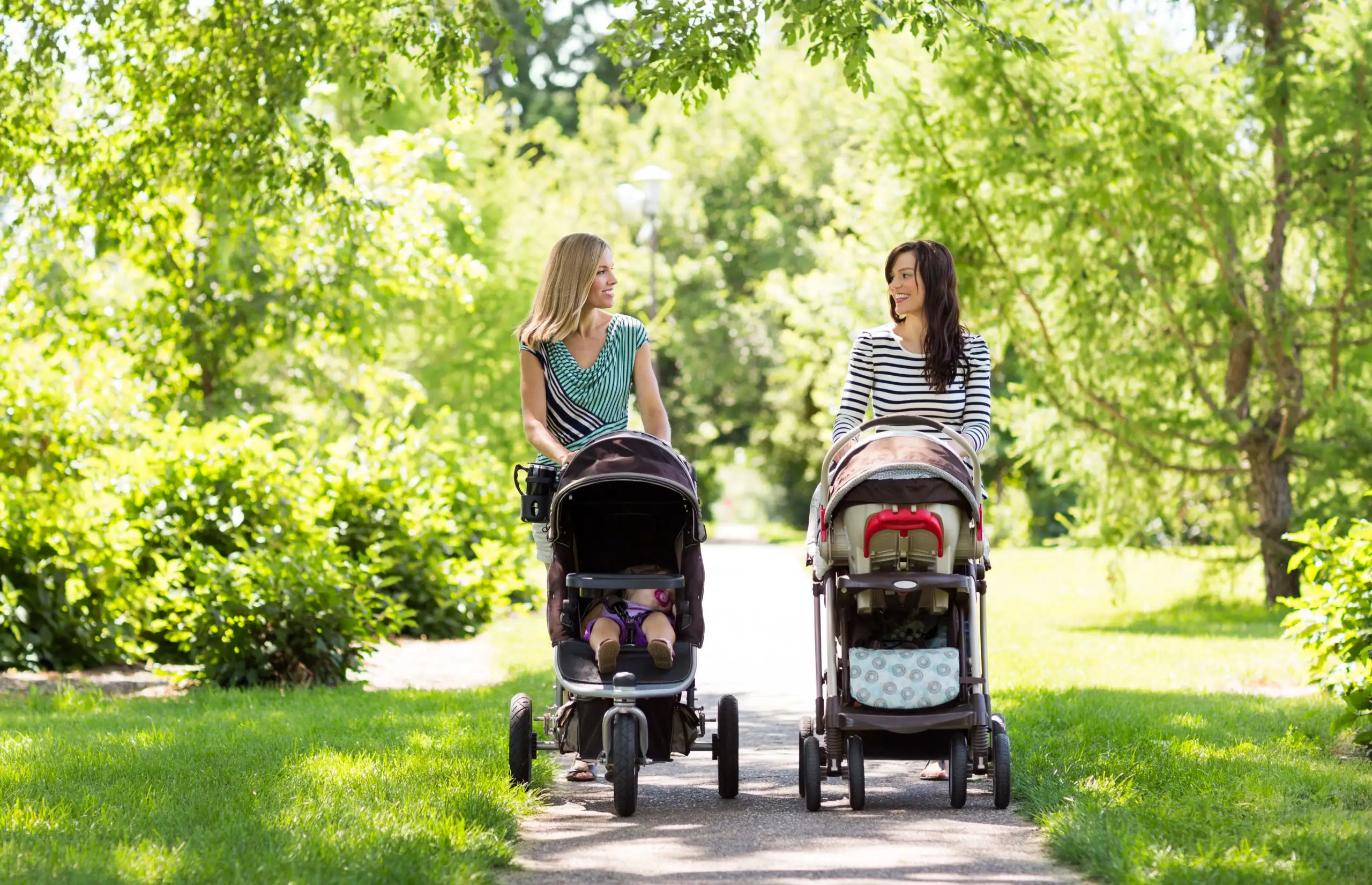 Two women pushing two babies in two strollers in the park