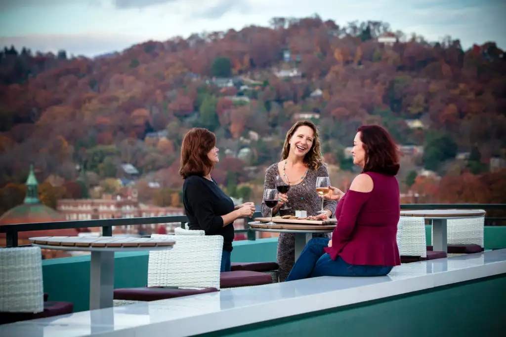 Three friends drinking wine on a patio overlooking fall foliage