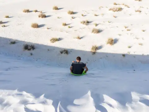 Man sliding down sand dune on sand sled