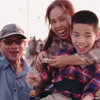 Two parents and a child in a wheelchair on the boardwalk by a beach