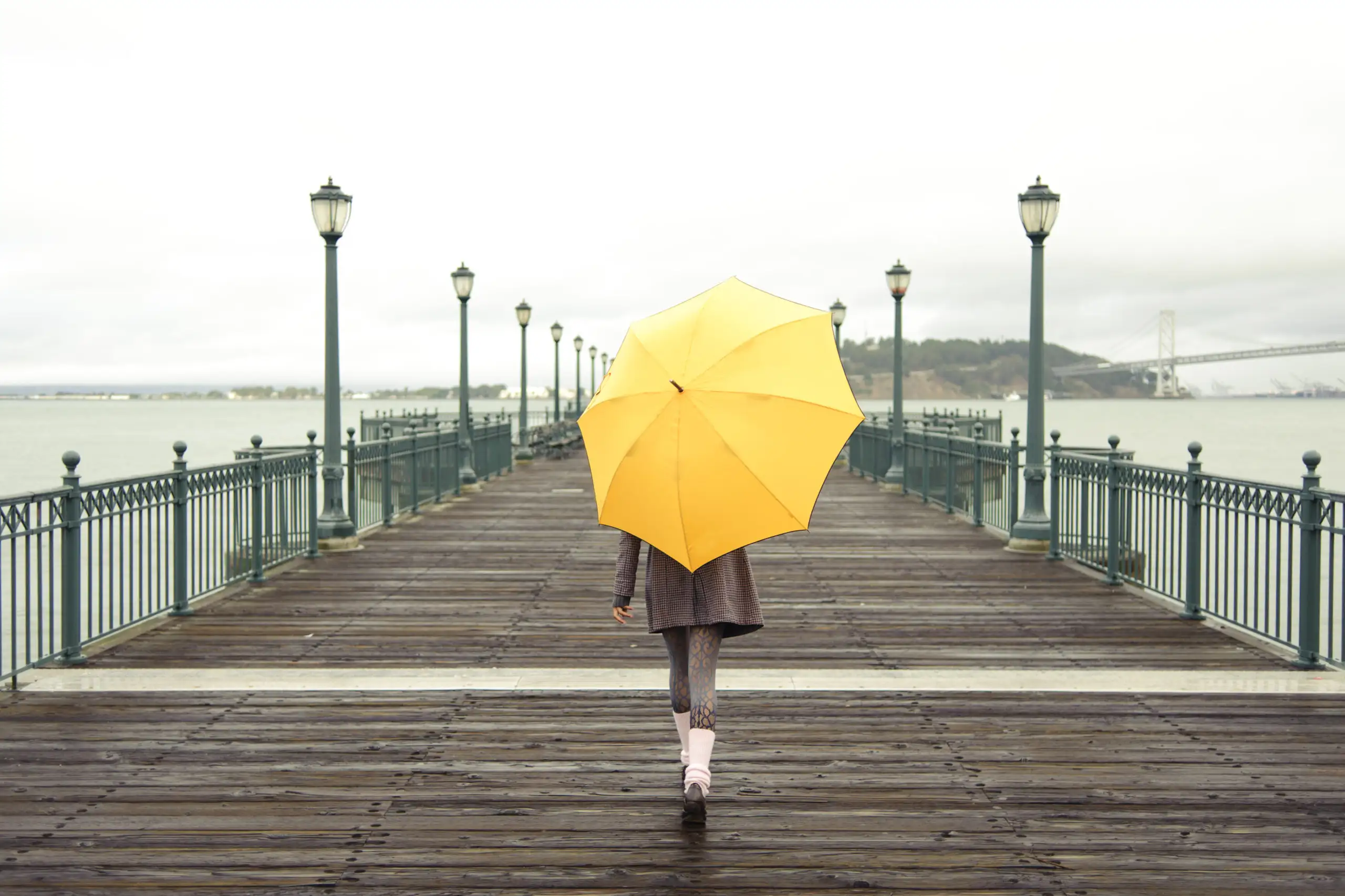 Woman carrying yellow umbrella and walking down a wooden boardwalk
