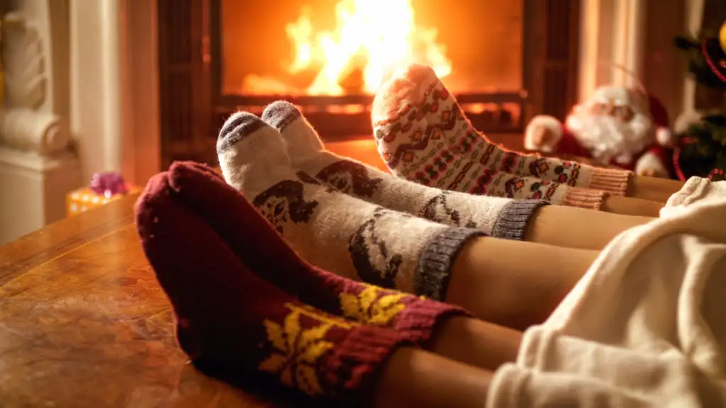 Close-up of three sets of feet wearing cozy socks in front of a lit fireplace