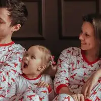 Family wearing matching holiday pajamas on a couch next to a Christmas tree