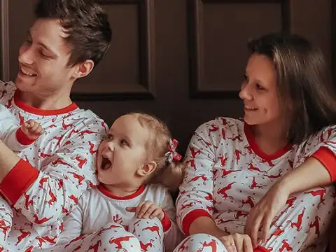 Family wearing matching holiday pajamas on a couch next to a Christmas tree